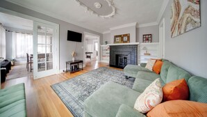 A living room with a green sofa, a fireplace, and a dining area with a table and chairs. - Deck, Pool Table! Walkable Cleveland Heights Apt (Cleveland Heights)