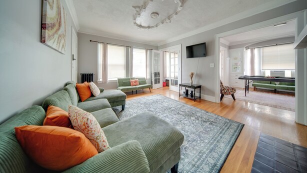 A spacious living room with a large green sofa, a patterned rug, and a television mounted on the wall. - Deck, Pool Table! Walkable Cleveland Heights Apt (Cleveland Heights)
