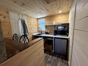 Eine kompakte Küche mit Holzwänden, einer Mikrowelle, einem Spülbecken und einem kleinen Kühlschrank.