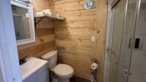 Une salle de bain aux murs lambrissés, équipée de toilettes, d’un lavabo et d’une douche.