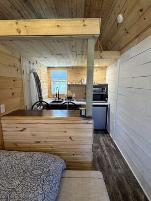 A compact cabin with a kitchenette, a dining area, and a sleeping space. - Cozy Tiny Cabin with Rustic Charm near Mineral Wells, Texas (Mineral Wells)