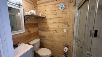 A wooden-paneled bathroom with a toilet, sink, and shower.