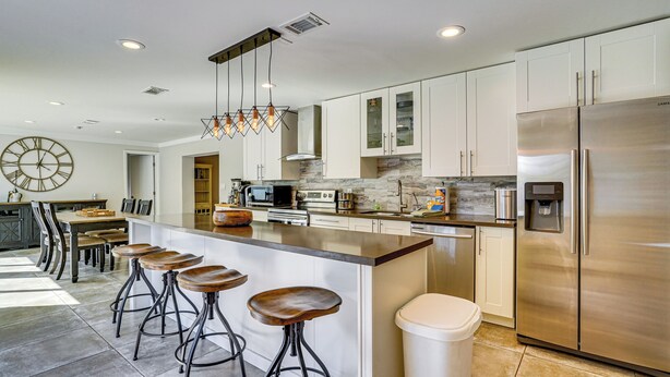 A modern kitchen with a central island, bar stools, stainless steel appliances, and a clock on the wall. - Convenient Oasis in St Pete, 4 Mi to Pier & Dtwn! (St. Petersburg)