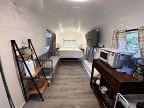 A compact, well-lit room with a bed, a TV, a microwave, and a small kitchenette area. - Charming Vintage Airstream with Covered Patio near Mineral Wells, Texas (Mineral Wells)