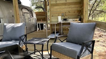 A wooden cabin with a covered patio, a dining table, and two grey cushioned chairs.