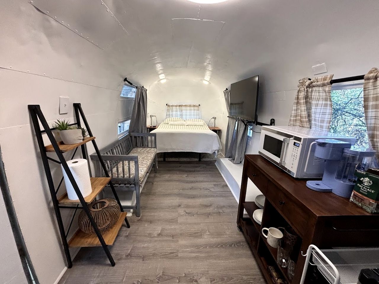 Una stanza compatta e ben illuminata con un letto, una TV, un forno a microonde e un angolo cottura.
