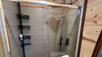 Cabina doccia in vetro con soffitto in legno, un portasci e una panca in legno con asciugamani.