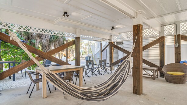 Un espacio al aire libre techado con una hamaca, mesas, sillas y un sillón de mimbre.