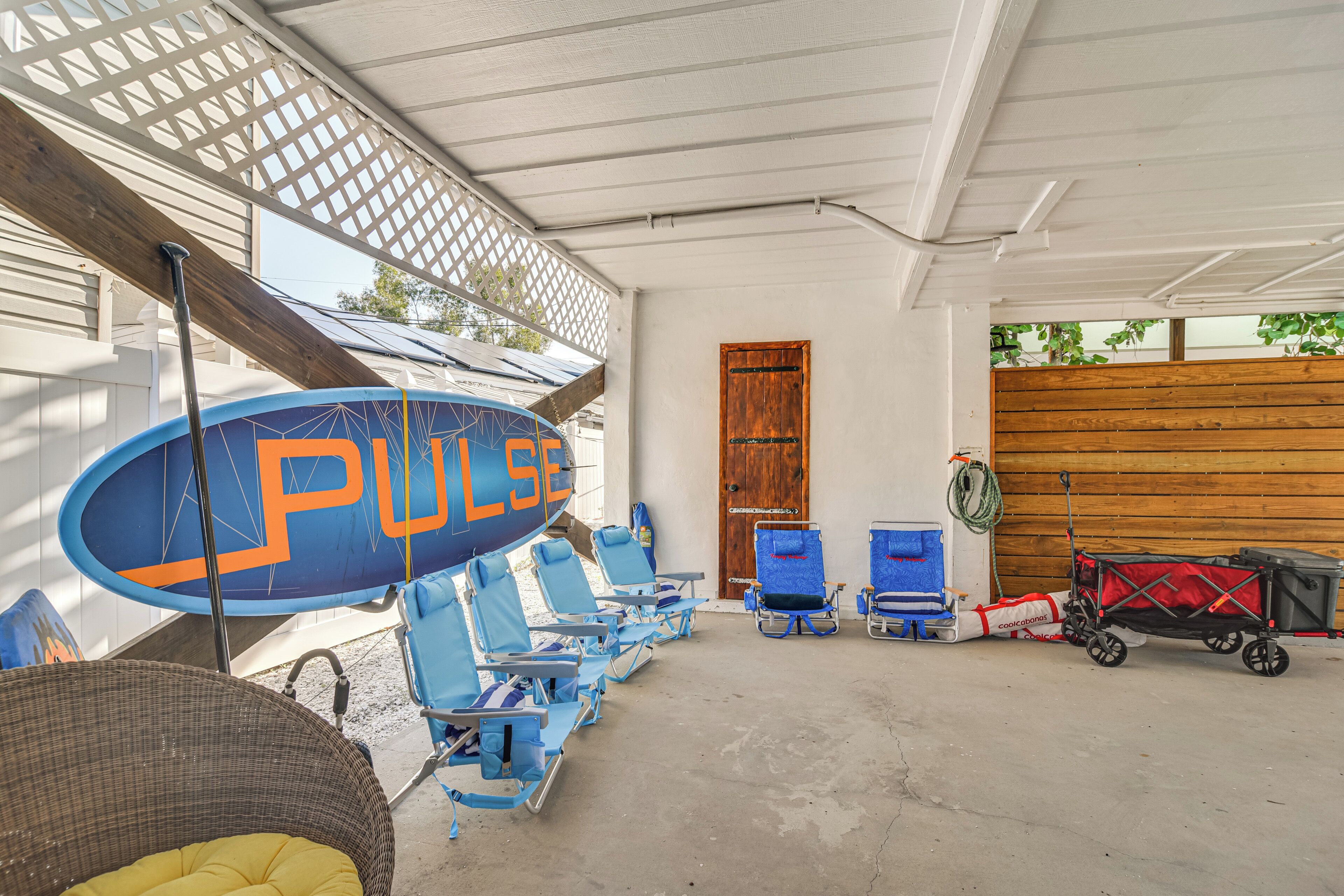 A covered outdoor area with blue lounge chairs, a wooden door, and a red and black stroller.