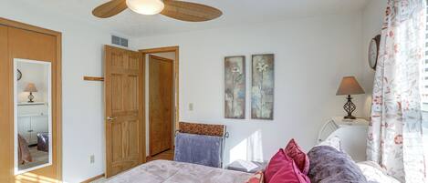 A bedroom with a bed, a ceiling fan, a door, a mirror, and a wall clock.