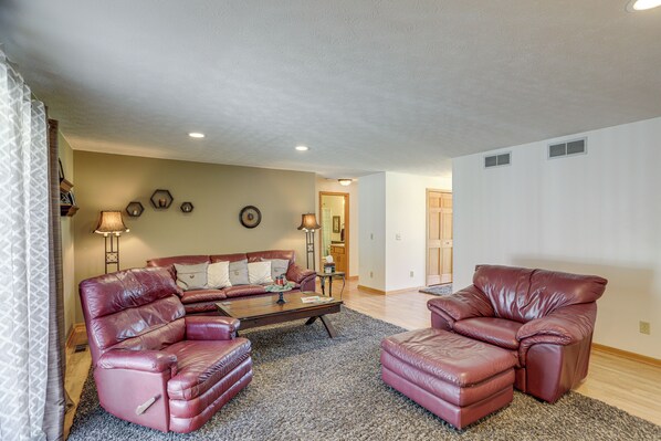 A living room with a leather sofa, a coffee table, and a rug. There is a lamp and a wall clock. - Work & Relax! Spacious Ontario Home w/ Pool (Mansfield)