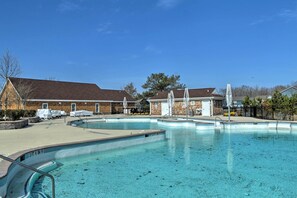 Ein Poolbereich mit klarem, blauem Pool, einem überdachten Sitzbereich und einem Gebäude mit braunem Dach im Hintergrund.