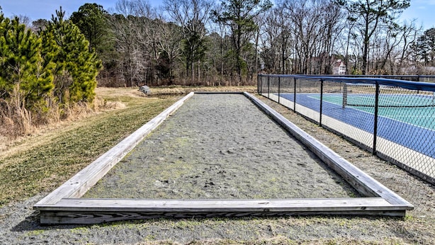 A tennis court with a wooden frame and net, surrounded by trees and a building in the background. - Game Room + Patio: Spacious Ocean View Home (Ocean View)