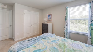 A bedroom with a bed, two white doors, a dresser, a window with curtains, and a ceiling fan. - Game Room + Patio: Spacious Ocean View Home (Ocean View)