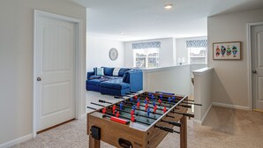 A room with a foosball table, a blue sofa, and a window with patterned curtains. - Game Room + Patio: Spacious Ocean View Home (Ocean View)