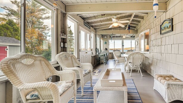 A covered outdoor seating area with wicker furniture, a ceiling fan, and large windows offering views of the outdoors. - River Access! Penobscot Retreat 5 Mi to Fort Knox (Stockton Springs)