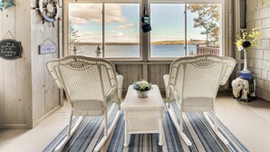 A room with a view of a lake, two wicker chairs, a small table, and decorative items like a ship's wheel and a sign saying "patch is my happy place". - River Access! Penobscot Retreat 5 Mi to Fort Knox (Stockton Springs)