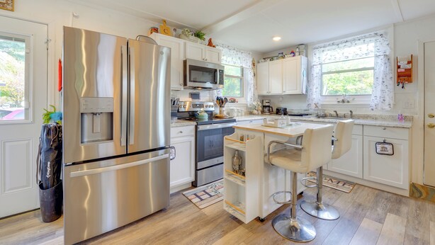 A modern kitchen with stainless steel appliances, white cabinetry, and a bar area with stools.