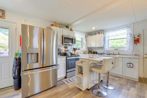 A modern kitchen with stainless steel appliances, white cabinetry, and a bar area with stools. - Bridge to Bay Adventure! Eastern Shore Cottage (Grasonville)