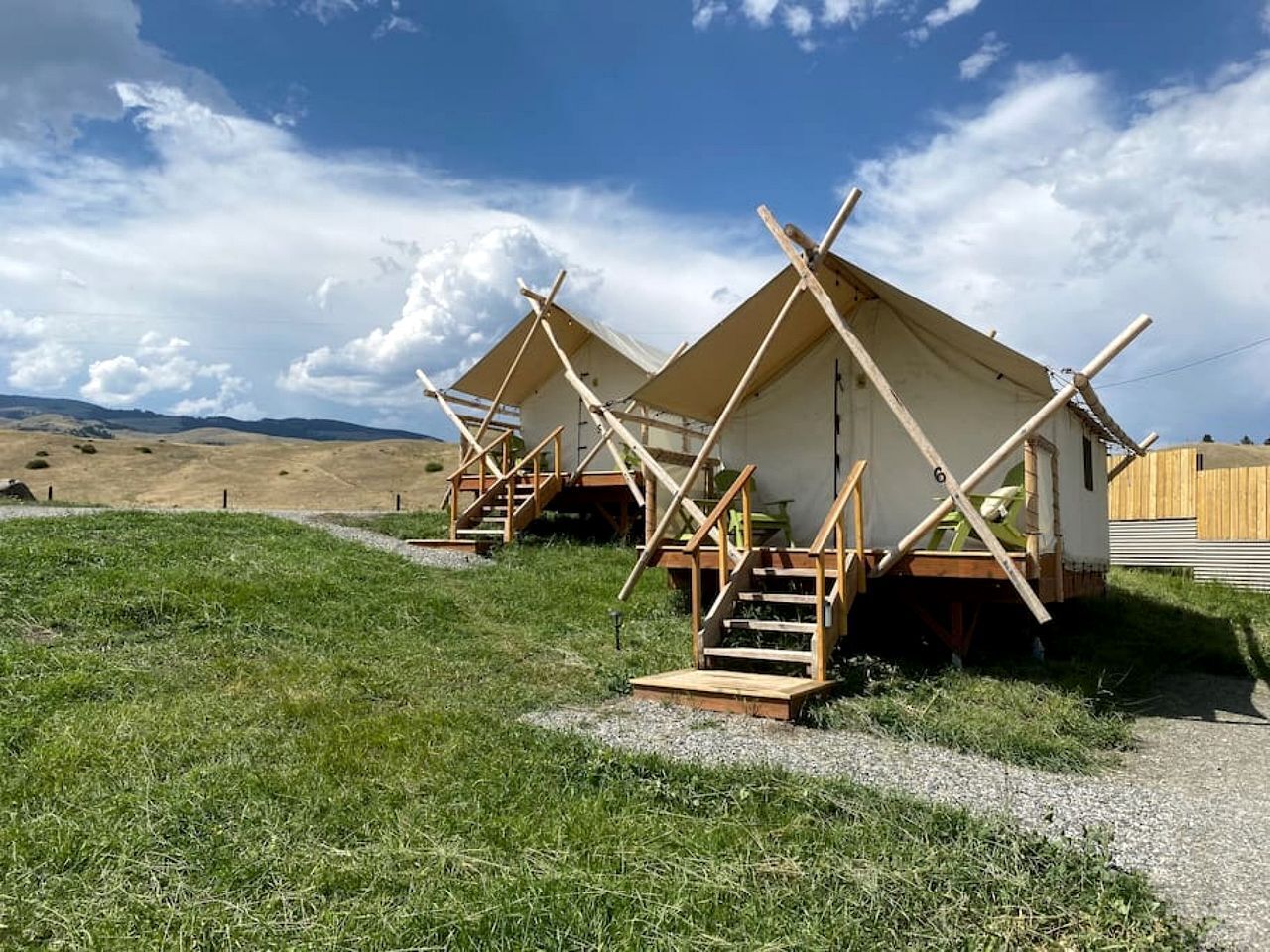 A series of wooden cabins with external staircases, set in a grassy field with a clear sky.