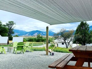 Ein überdachter Außenbereich mit Bergblick, einem Picknicktisch und grünen Stühlen.