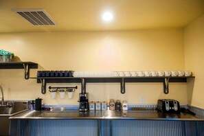 Una cocina con encimera de acero inoxidable, cafetera, tostadora y estantes con tazas y frascos.