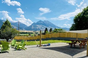 An outdoor seating area with chairs and a table, a wooden fence, and a mountain view.