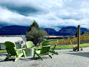 Une terrasse en gravier avec quatre chaises Adirondack vertes, une table en métal et une clôture en bois en arrière-plan.