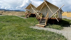 A series of wooden cabins with external staircases, set in a grassy field with a clear sky.