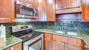 Uma cozinha com armários de madeira, micro-ondas de aço inoxidável, fogão e bancada de granito.