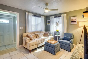 Una sala de estar con sofá, reposapiés, sillón y ventilador de techo.