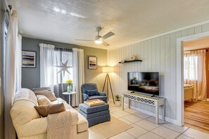 Una sala de estar con sofá, reposapiés, sillón, televisor y ventilador de techo.