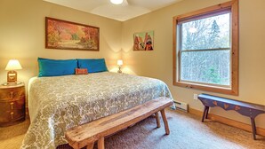 A bedroom with a bed, a bench, a ceiling fan, a window, and wall art.