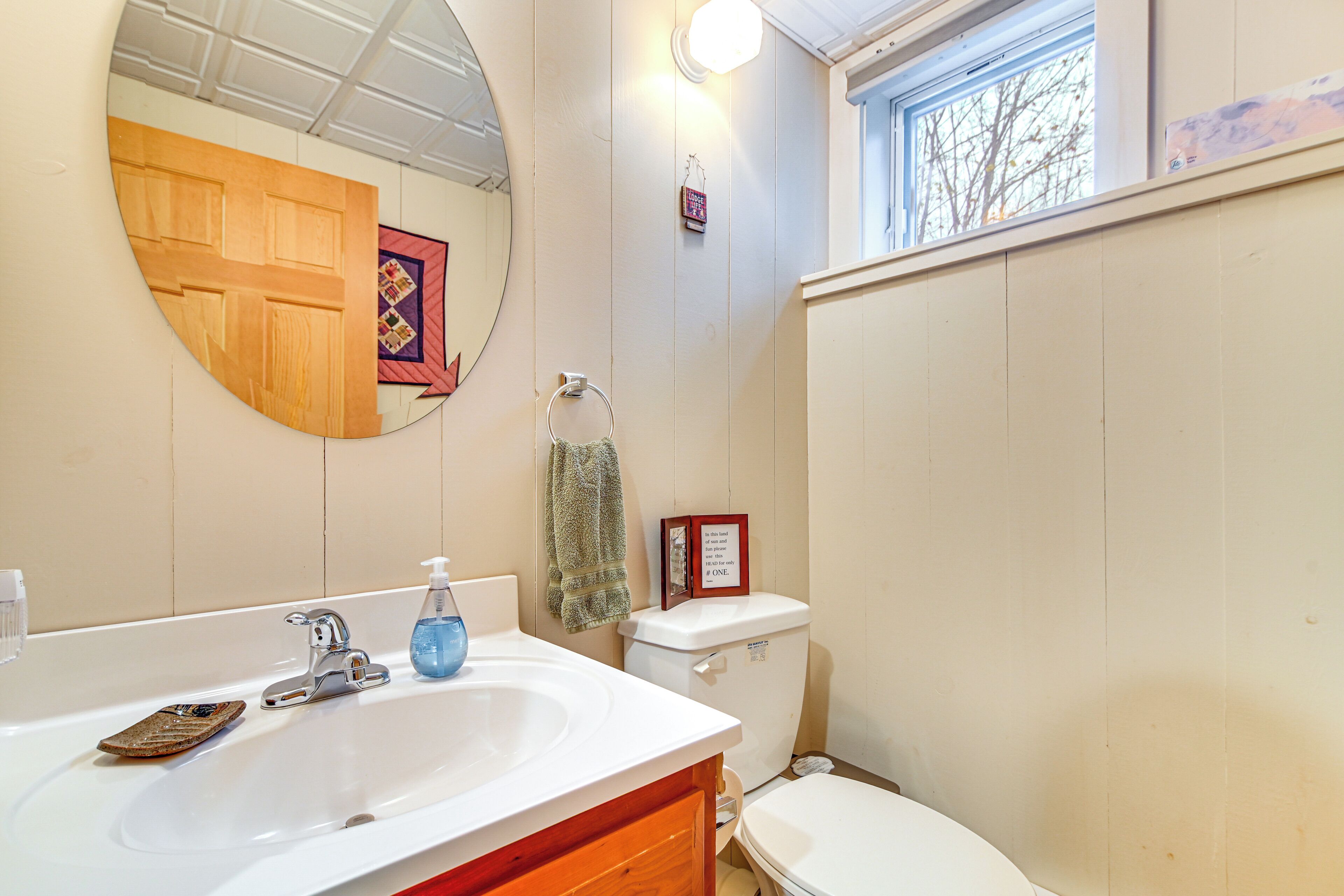 Une salle de bain avec un lavabo blanc, un miroir, des toilettes et une fenêtre.
