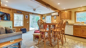 A cozy cabin interior with a dining area, wooden furniture, and large windows offering a view of the outdoors.