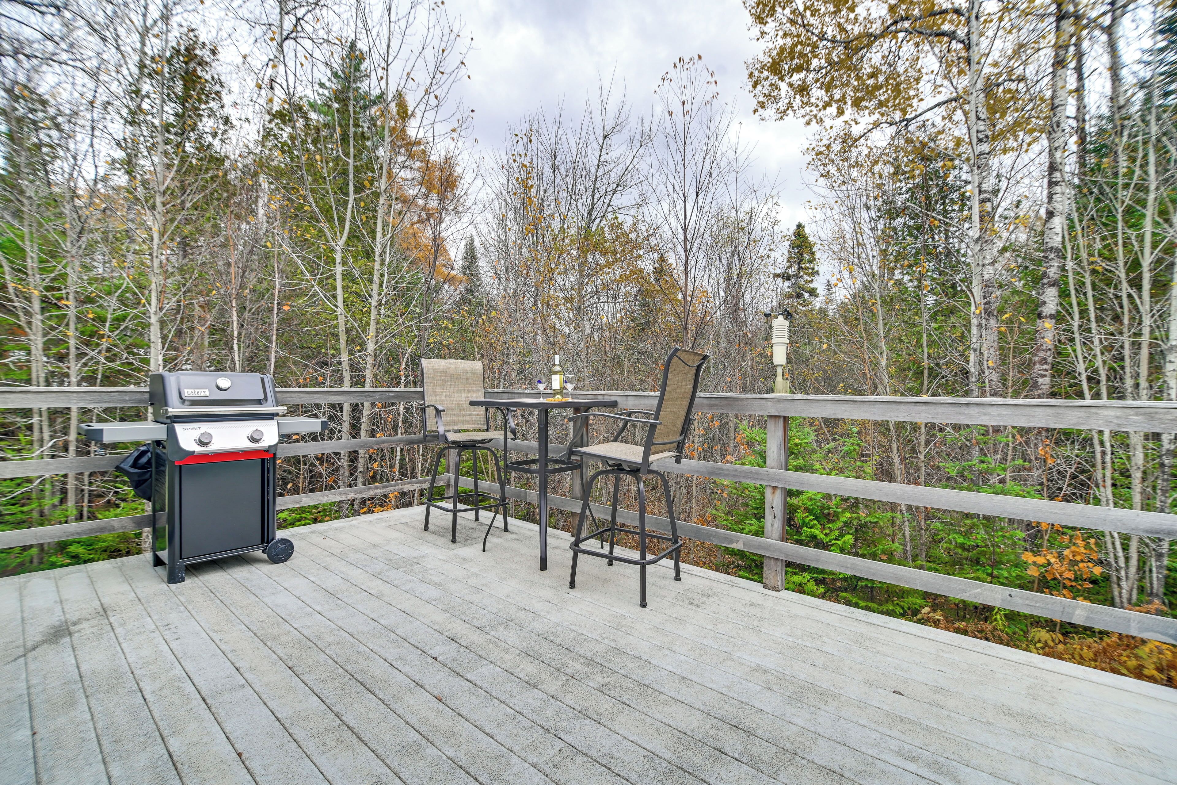 An outdoor deck with a grill, two chairs, and a table.