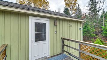 A small, single-story building with a green exterior, a white door, and a wooden deck with a lattice railing.