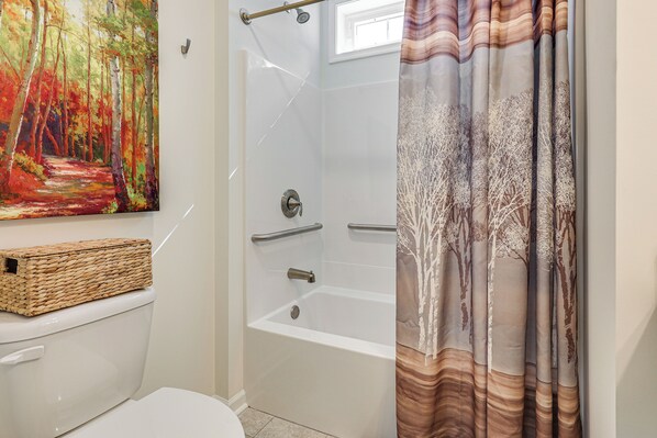 Ein Badezimmer mit Dusche, Toilette und einem Bild von einem Waldweg.