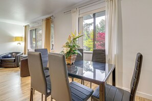 A dining area with a glass table, leather chairs, a potted plant, and large windows with curtains. - Quiet, Pet Friendly! Bothell Apt Near Wine Country (Mill Creek)