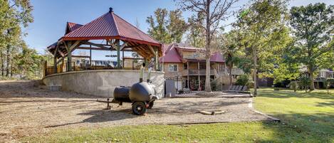 Un espacio al aire libre techado con una parrilla, un pabellón de madera y un edificio con techo rojo.