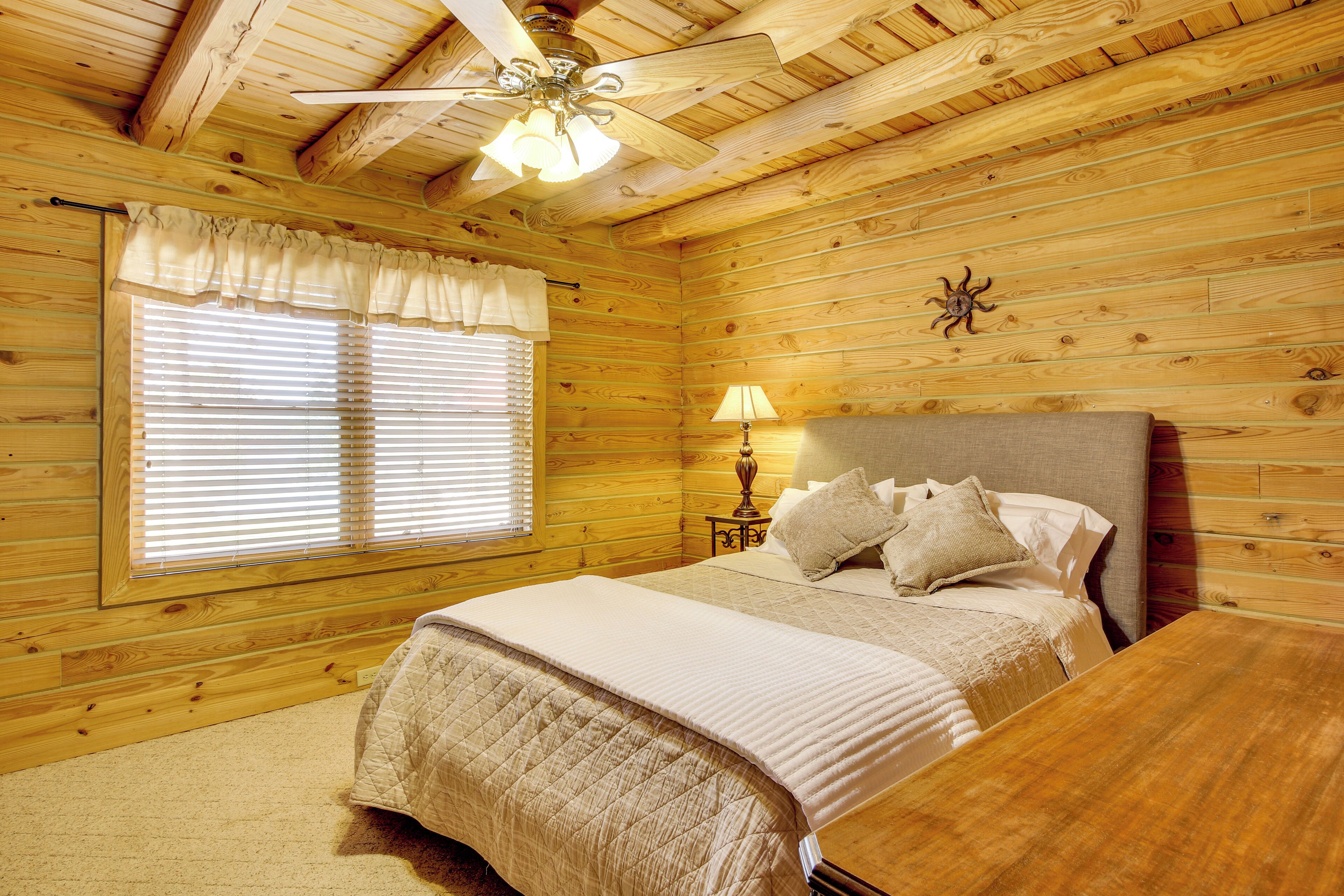 A wooden cabin bedroom with a bed, a nightstand, a lamp, and a ceiling fan.