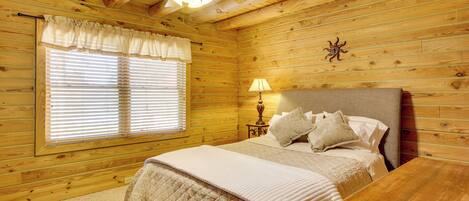 A wooden cabin bedroom with a bed, a nightstand, a lamp, and a ceiling fan.