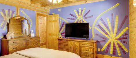 Une chambre à coucher avec un lit, une commode en bois, un téléviseur et un ventilateur de plafond.