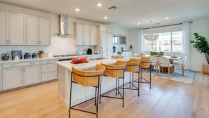 A modern kitchen with white cabinetry, a central island with bar stools, and a dining area with a table and chairs. - Elegant & Spacious Retreat w/ Yard in Woodland! (Woodland)