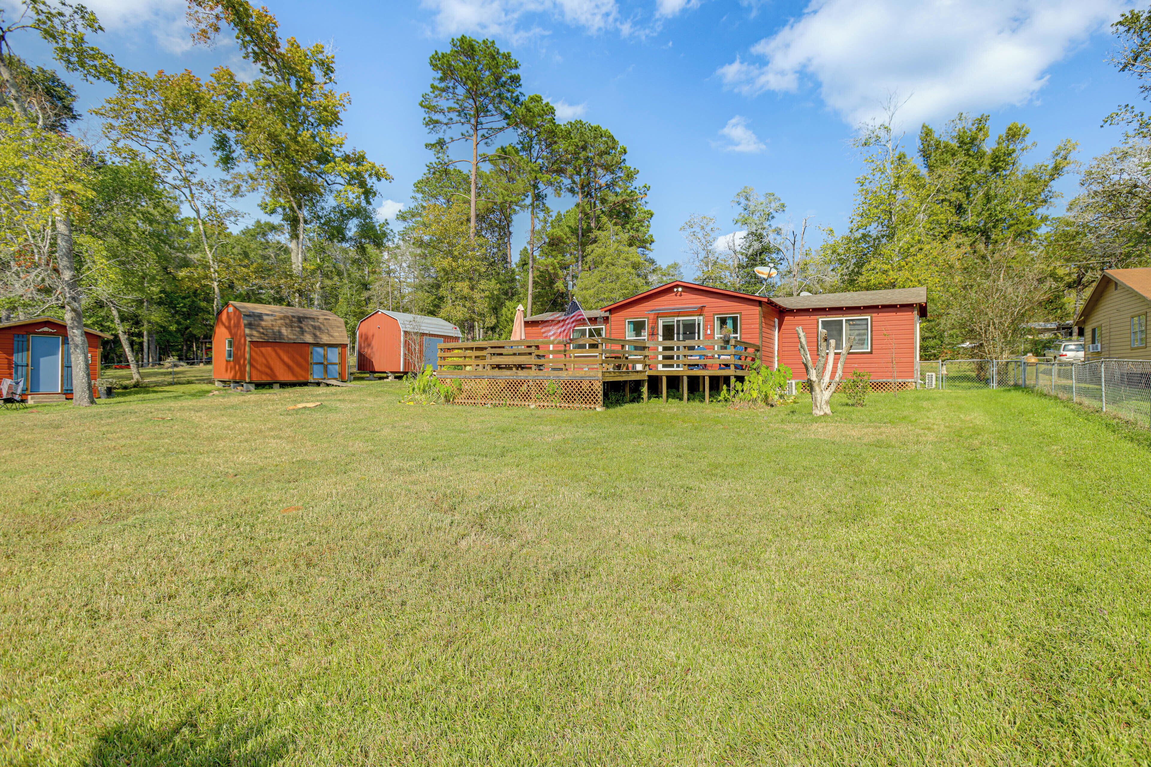 A red cabin with a deck, surrounded by a grassy yard and trees.