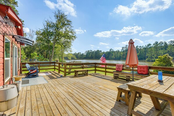 A wooden deck with a view of a lake, a red building, and a flag.