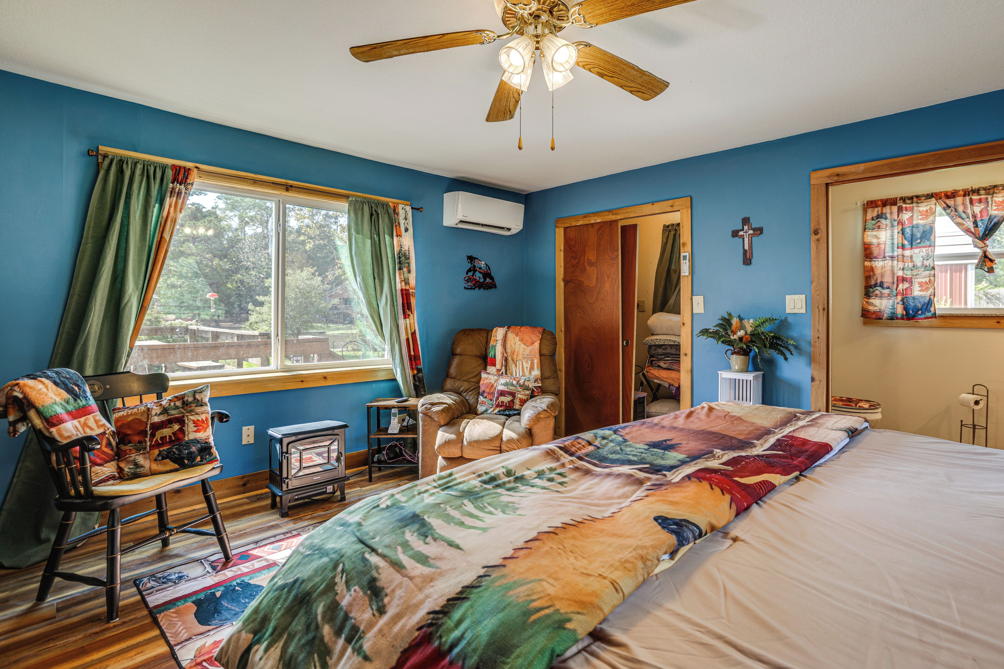 Ein Schlafzimmer mit einem großen Bett, einem Sessel mit Decke, Holzboden, Deckenventilator und einem Fenster mit Vorhängen.