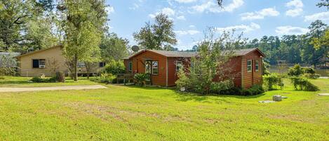 A two-story cabin with a front porch and a small deck, surrounded by a well-maintained lawn and trees.