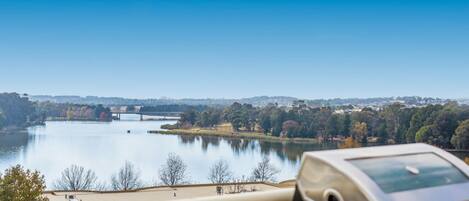 A view of a lake with a bridge, trees, and buildings in the background.