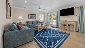Un salon avec un tapis à motifs bleus, un ventilateur de plafond, un téléviseur à écran plat et un bureau avec une chaise.